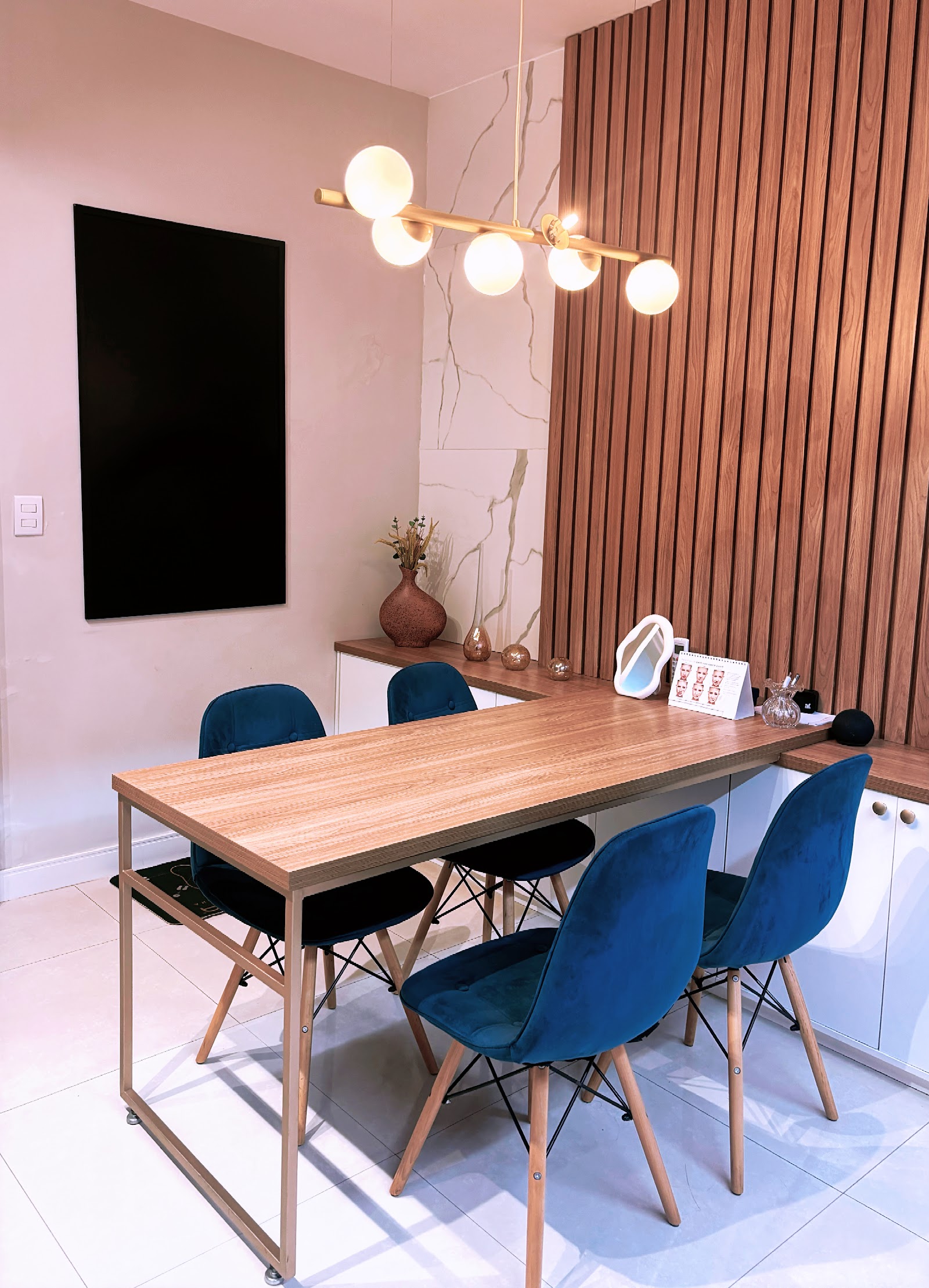 Sala de avaliação com mesa de madeira, cadeiras azuis, parede ripada e luminária de globos