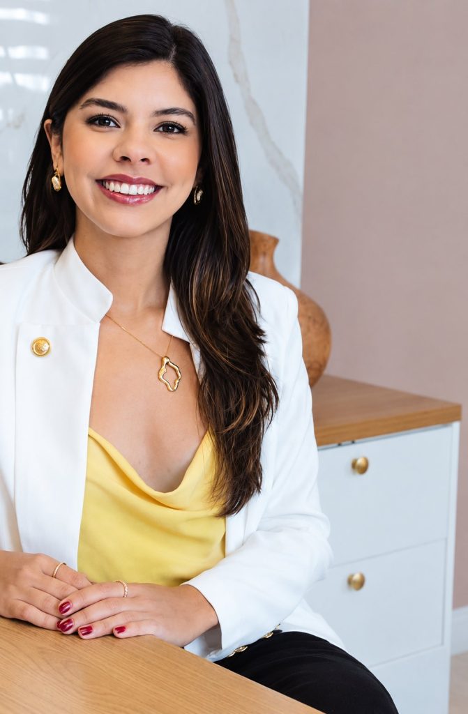 Dra. Kethelin Oliveira de blazer branco à mesa do consultório