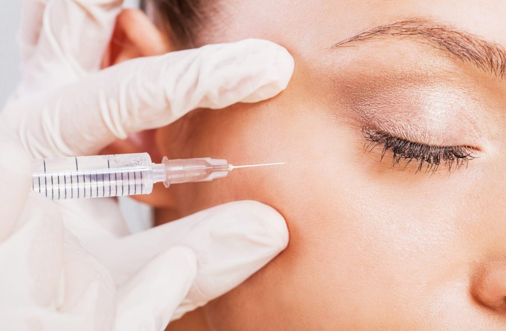 Mãos com luvas brancas aplicando toxina botulínica próximo aos olhos